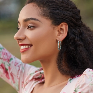 Boucles d'oreilles créoles torsadées argentées avec zircons verts sur un mannequin