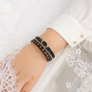 Detail of multi-layer layered bracelet with black beads and gold-trimmed gemstone charm