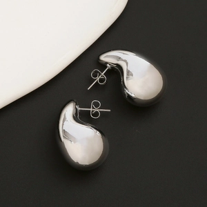 Primer plano de pendientes de gota en plata pulida sobre fondo minimalista texturizado