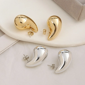 Vista detallada de pendientes de gota en oro y plata con textura de metal pulido brillante