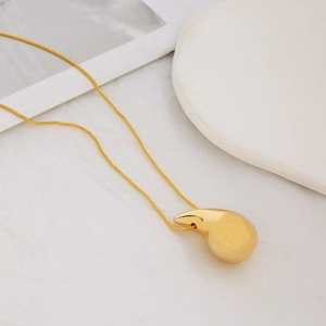 Detalle de un collar dorado con colgante de gota minimalista sobre fondo de mármol blanco