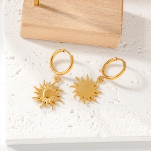Close-up of golden sun pendant earrings on white textured background with wooden decor