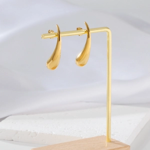 Boucles d'oreilles pendantes dorées pour femmes sur un socle en pierre et bois épuré