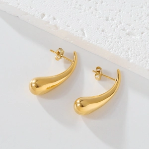 Vue détaillée des boucles d'oreilles gouttes dorées polies sur fond de pierre blanche