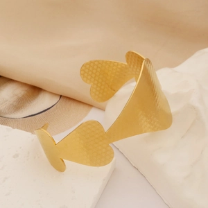 Close-up of golden hollow cuff bracelet with heart patterns on white stone steps