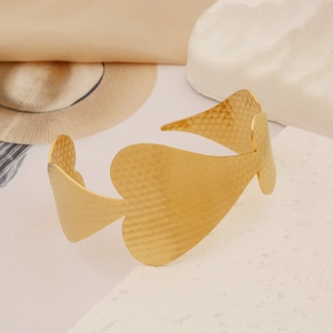 Detailed view of golden heart-shaped bangle with textured finish on stone background