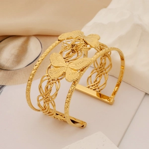 Detailed close-up of golden hollow butterfly and floral patterns on a wide cuff bracelet