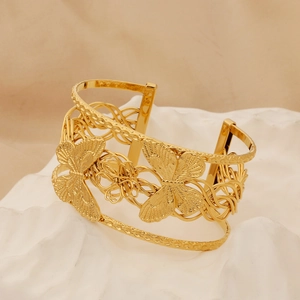 Detailed macro shot of a golden hollow butterfly cuff bracelet on white decorative stones