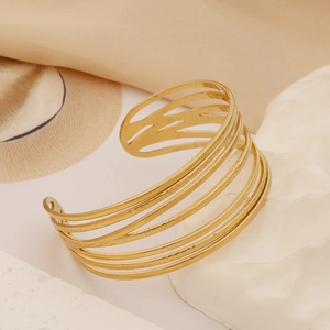 Detail shot of a golden multi-layer镂空 hammered cuff bracelet on white stone