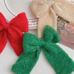 Detail of handmade knit Christmas bow hair clips with gold thread and long ribbon tails