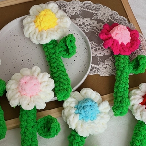 Close-up of handmade crochet chamomile flowers with knitted petals and green stems