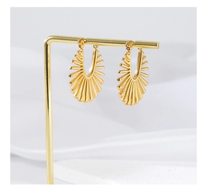 Detail of gold fan-shaped earrings with sunburst texture hanging on a minimalist display stand