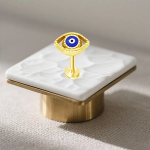 Dettaglio macro di piercing labret occhio di Allah dorato con resina blu su base bianca