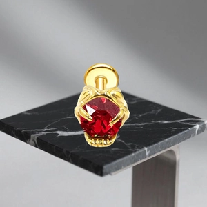Detailed view of G23 titanium ear stud with red gemstone and golden bat wing claw setting