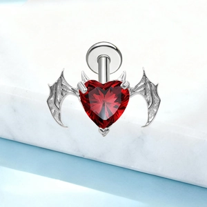 Detailed macro view of heart-shaped red gemstone stud with silver bat wings on marble