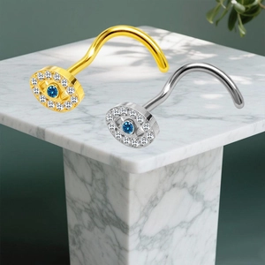 Detailaufnahme von Gold und Silber Evil Eye Nasenpins mit blauen Kristallen auf Marmor