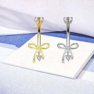 Dettaglio di piercing all'ombelico con fiocco e ciondolo a cuore in oro e argento