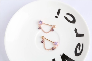 Detail of rose gold nipple rings with purple star crystals and beaded chains on ceramic