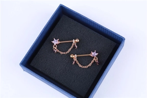 Detail of rose gold piercing jewelry with purple star zircon and teardrop chain charms