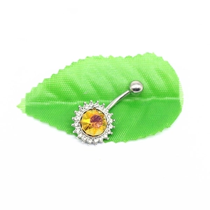 Macro shot of silver sunburst belly ring with orange gemstone on a green leaf background