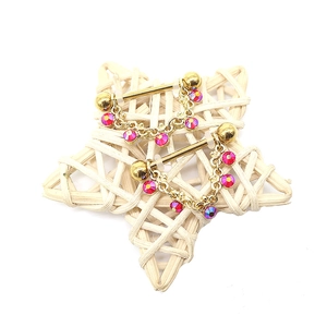 Macro-detail van vergulde tepelpiercings met rozerode kristallen en hangende ketting