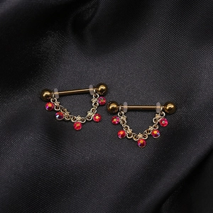 Gouden tepelpiercings met hangende kettingwaaiers en fonkelende rode strassteentjes