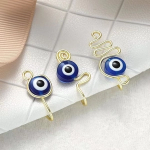 Macro detail of three handmade gold wire evil eye clip-on nose rings on white leather