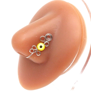 Macro shot of silver wire-wrapped nose ring clip with yellow evil eye on silicone model