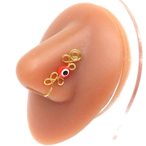 Macro detail of a golden spiral non-piercing nose ring featuring a red evil eye bead