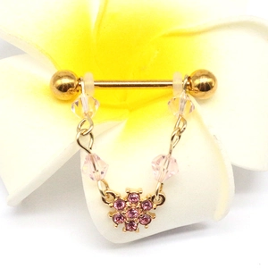 Golden flower nipple ring with pink crystals and beaded chain on a floral background