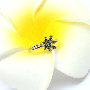 Macro shot of maple leaf non-pierced nose ring with green crystals on a plumeria flower