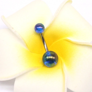 Détail macro du piercing de nombril acrylique bleu iridescent sur fond floral blanc