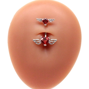 Dettaglio di un piercing all'ombelico in acciaio inossidabile con cuore rosso e ali