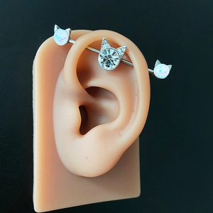 Detailed view of cat-themed industrial barbell with opal and cubic zirconia on ear model