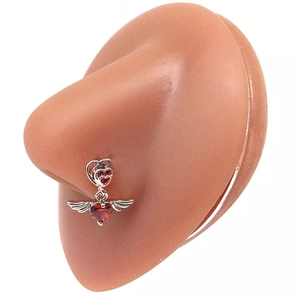 Dettaglio macro di un piercing al naso in argento con rubino rosso a cuore e ali d'angelo
