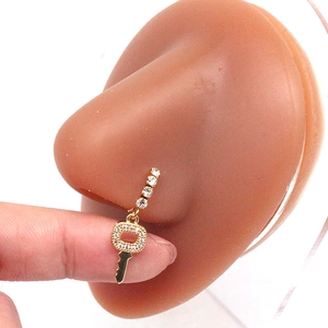 Macro-opname van gouden neuspiercing met een rij zirkonia en een sleutelvormige hanger aan het sieraad