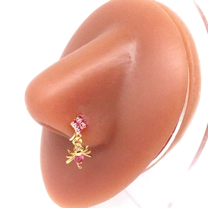 Detail of a gold nose ring with pink stones and a dangling spider charm on a nose model