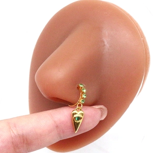 Detail of gold nose ring with green crystals on a silicone nose model for scale