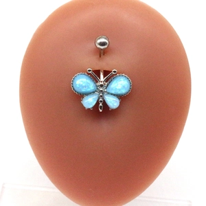 Détail d'un piercing de nombril papillon argenté avec des opales bleu clair sur un modèle