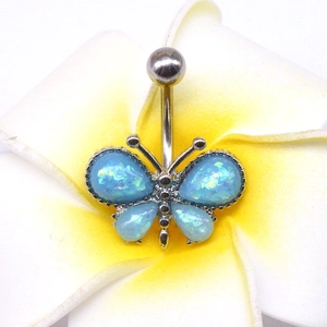 Détail du piercing de nombril papillon avec ailes en opale bleue sur une fleur frangipanier