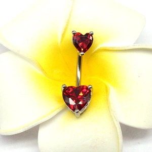 Gros plan du piercing de nombril en cœur avec zircon rouge sur une fleur tropicale