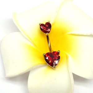 Vue détaillée du piercing de nombril coeur doré avec zircon rouge sur une fleur blanche