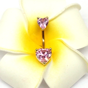 Détail macro d'un piercing nombril cœur doré avec zircons roses sur une fleur de frangipanier