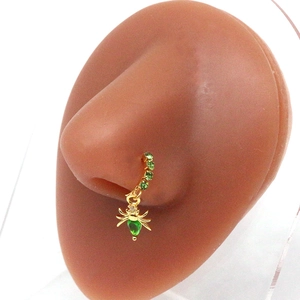 Detail showing a gold nose ring with a spider pendant and green gemstone accents