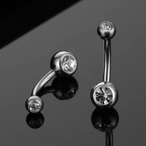 Macro view of silver G23 titanium belly rings with clear crystals on black reflective background
