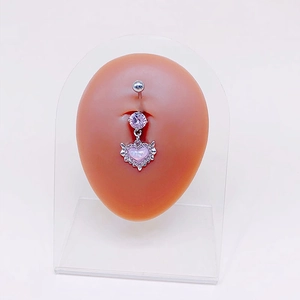 Detail view of heart belly ring with pink opal wings on human skin silicone model