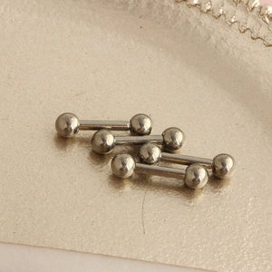 Close-up of three polished G23 titanium barbell studs on a textured beige jewelry display