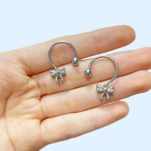 Détail d'anneaux de mamelon argentés avec nœud et zircon rose en design fer à cheval