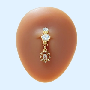 Nahaufnahme eines vergoldeten Bauchnabelpiercings mit Zirkonia-Steinen auf Hautmodell