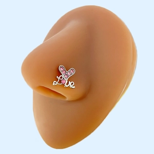 Detail showing a heart-shaped nose stud with pink crystals and Love script on a model